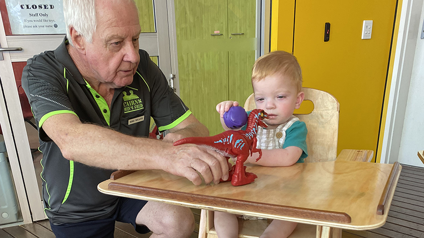 Cairns Men's Shed member Mike Wraith with 12-month-old Levi, testing out Cairns Hospital's paediatric ward's new Patsy high chairs